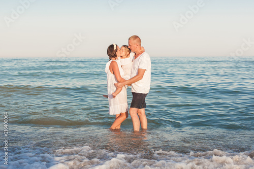 Parents with a daughter stand on the seashore and embrace.