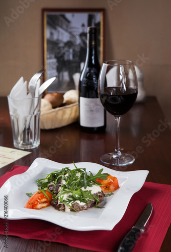 Meat with arugula on a white plate with a glass of red wine in a restaurant