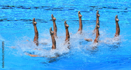 Synchronized Swimmers point up out of the water in action. Synchronized swimmers legs movement. Synchronized swimming team performing a synchronized routine of elaborate moves in the water.