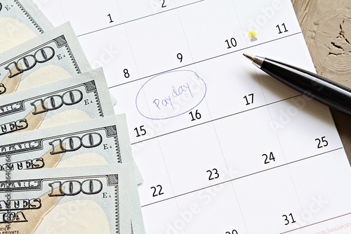 Business, finance, savings money, wages, payroll or accounting concept : Calendar with blue marker circle in word payday and American dollars cash money for remind photo