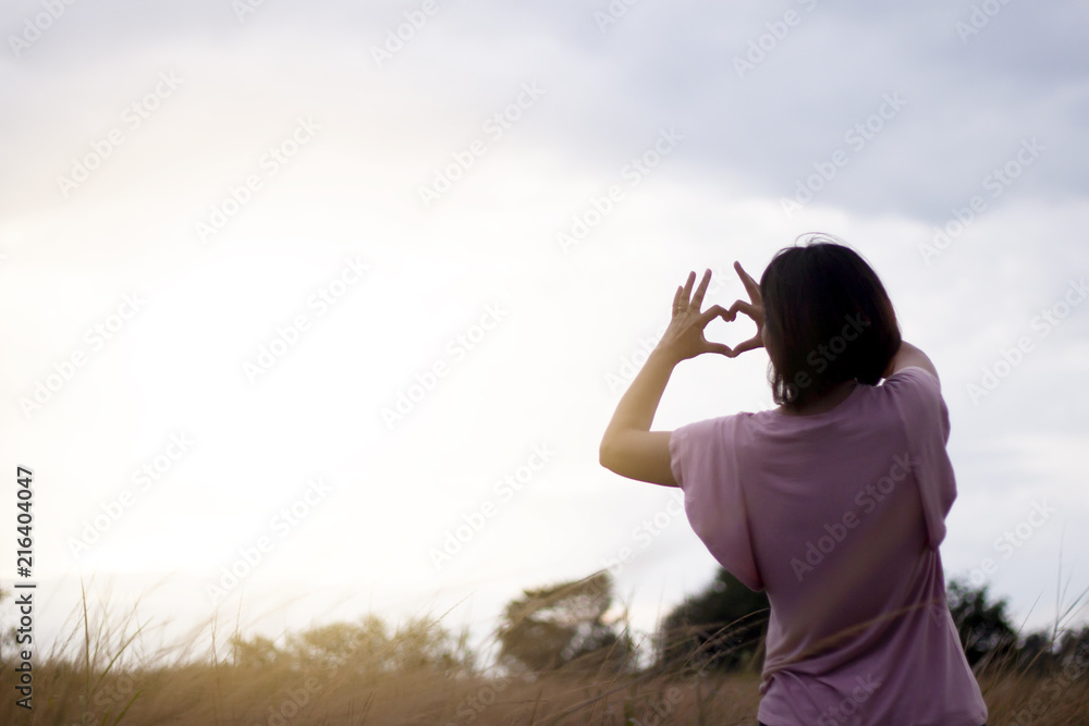 Relax time of women walk and show hand heart shape on highly covered meadow evening.