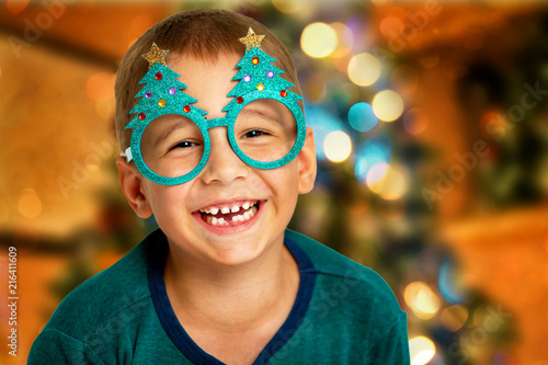 Portrait of a happy child on a christmas tree background. Smiling boy with glasses close-up