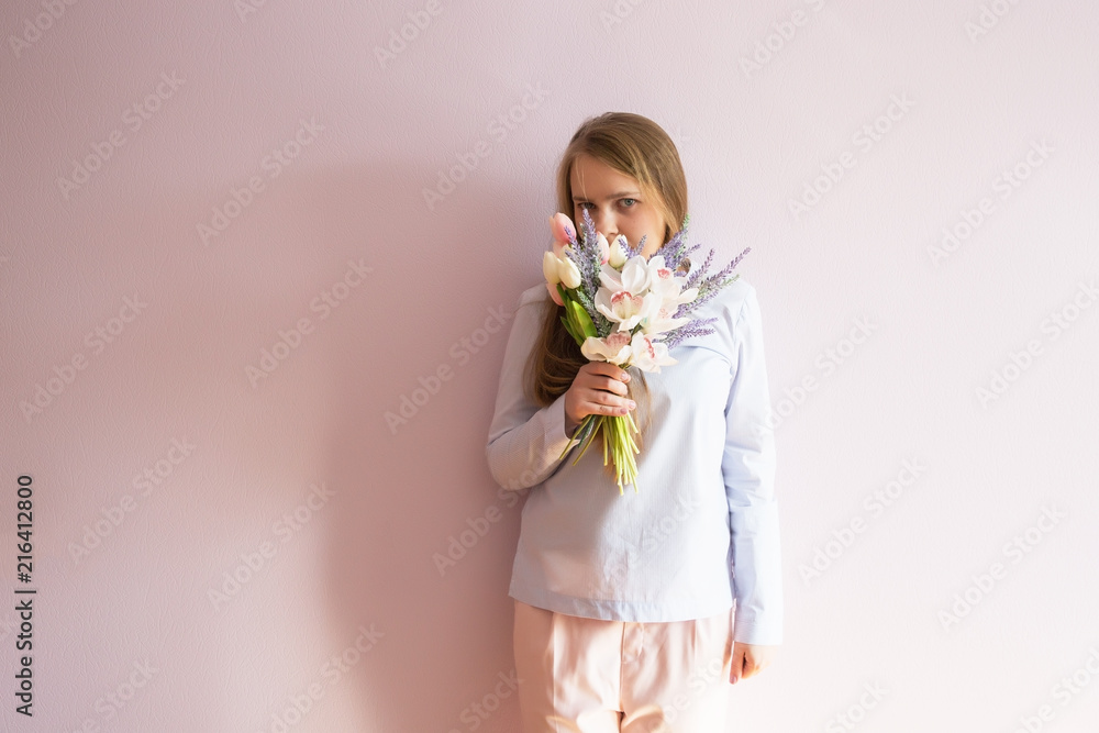 A young beautiful girl with blond dissolved long hair, a felt hat on her head, keeps spring flowers in her hands on a sunny day. Women's Day. A young beautiful girl with blond dissolved long hair, a felt hat on her head, keeps spring flowers in her hands on a sunny day. Women's Day.