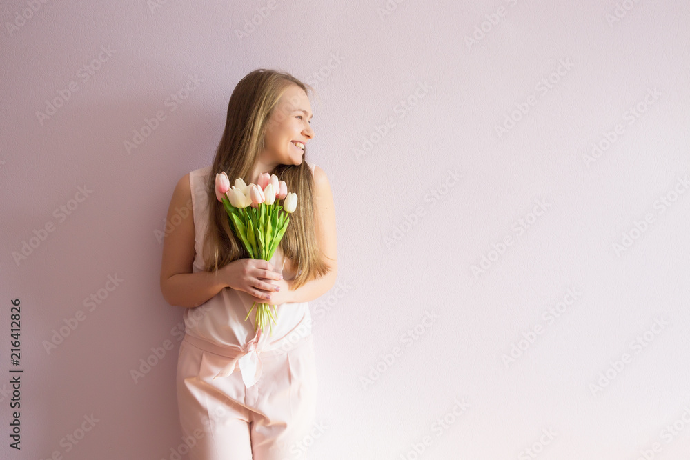 A young beautiful girl with blond dissolved long hair, a felt hat on her head, keeps spring flowers in her hands on a sunny day. Women's Day. A young beautiful girl with blond dissolved long hair, a felt hat on her head, keeps spring flowers in her hands on a sunny day. Women's Day.