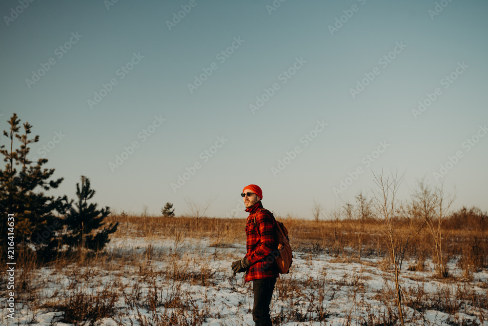 Tourist standing alone outdoor in black sunglasses, orange cap and red plaid shirt, jacket. Travel lifestyle and emotions concept. Film effects colors. Wanderlust, hiking. Winter holiday. Christmas.