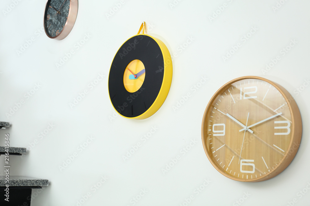 Different stylish clocks hanging on white wall. Time of day Different stylish clocks hanging on white wall. Time of day