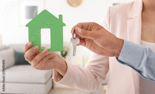 Young couple holding key and house model, closeup. Real estate agent services