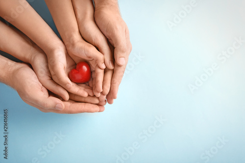 Canvas Print Family holding small red heart in hands on color background