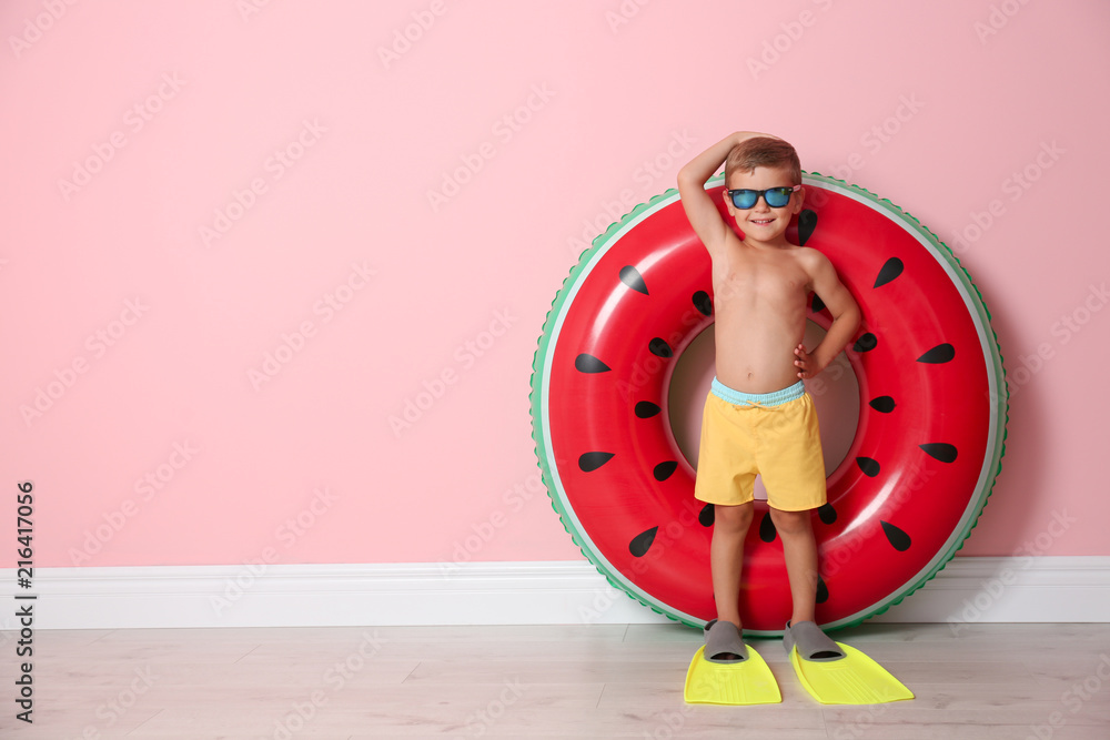 Fototapeta premium Cute little boy with inflatable ring wearing flippers near color wall