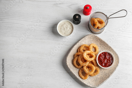 Plate with tasty onion rings and sauces on table, top view