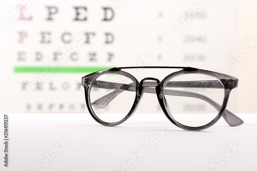 Glasses with corrective lenses on table against eye chart