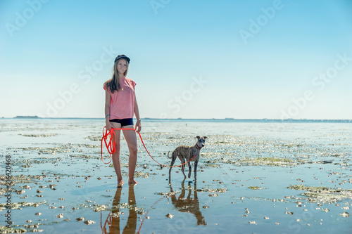 junges blondes Mädchen läuft mit ihrem Whippet Hund im Wattenmeer