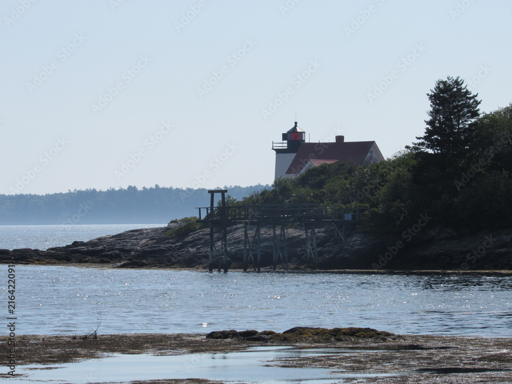 View of Hendricks Head Lighthouse in Southport, Maine behind trees and plants in the summer 