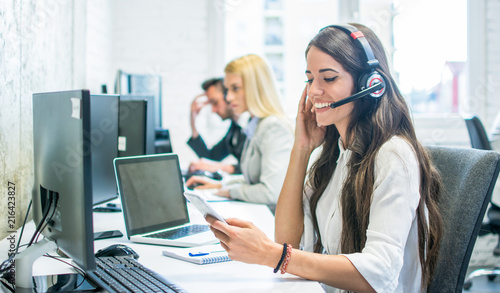 Friendly female customer support operator with headset using phone in office photo