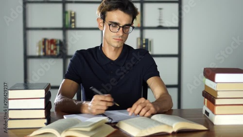 Concentrated student studying at home. Preparing for the university, learning, education and school concept. Man with books or textbooks writing to notebooks photo