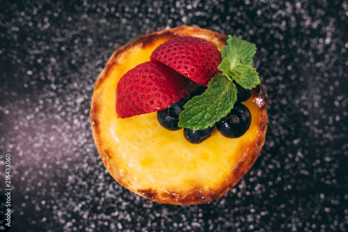 Close up Cheese tart topping with slices of strawberry and blackberry with icing sugar.
