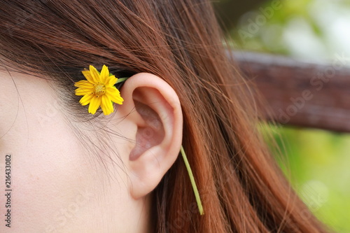 Close up small yellow flower on young woman ear