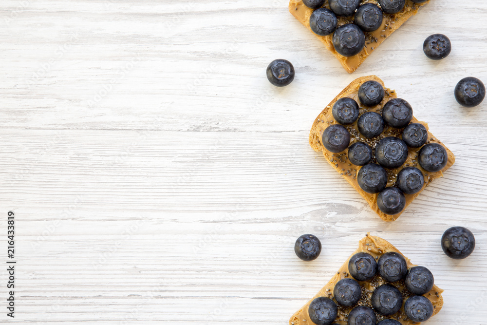 Vegan toasts with peanut butter, blueberries and chia seeds on a white wooden background, top view. Healthy eating. Flat lay, from above. Space for text. Vegan toasts with peanut butter, blueberries and chia seeds on a white wooden background, top view. Healthy eating. Flat lay, from above. Space for text.