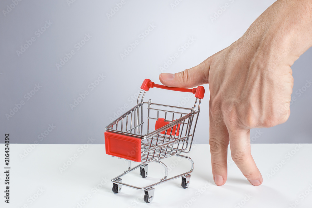 Fototapeta premium Male hand standing on two fingers and holding shopping cart on white background