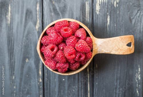 Obraz na plátně Wooden bowl with summer raspberries on black table close up