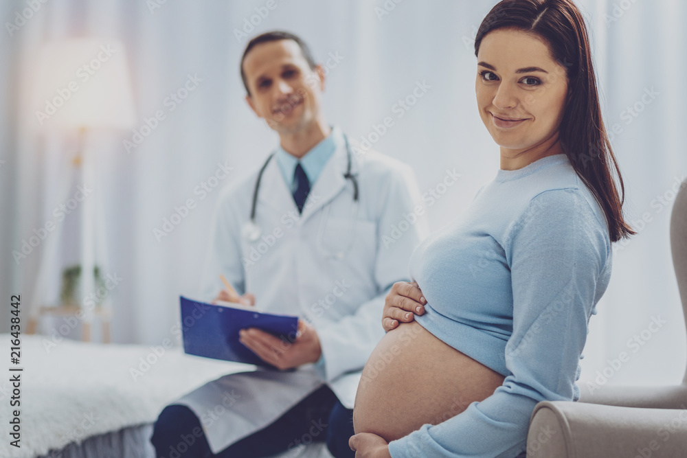 Cheerful smile. Delighted pregnancy visiting her doctor and keeping smile on face Cheerful smile. Delighted pregnancy visiting her doctor and keeping smile on face