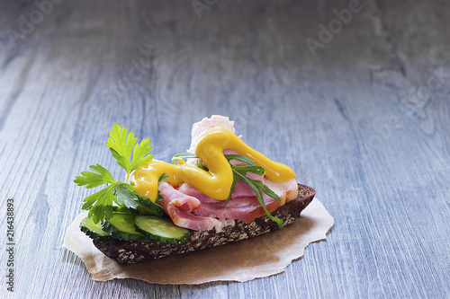 Sandwich with ham, fresh cucumber and mustard on brown paper.