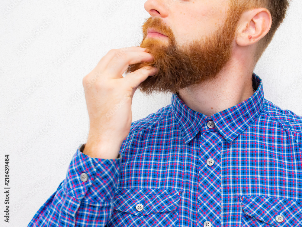 young man in a flannel shirt touches with hand his beard young man in a flannel shirt touches with hand his beard
