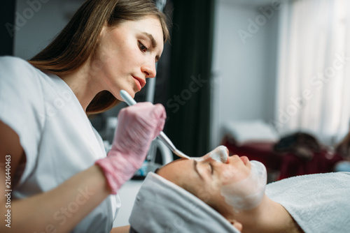 Doctor in gloves rubs the cream on patient face photo