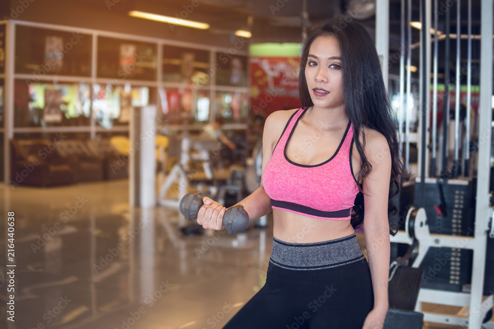 Sport girl does exercises with dumbbell on right hand in fitness gym blurred background, woman in sportswear, sport and exercises Sport girl does exercises with dumbbell on right hand in fitness gym blurred background, woman in sportswear, sport and exercises