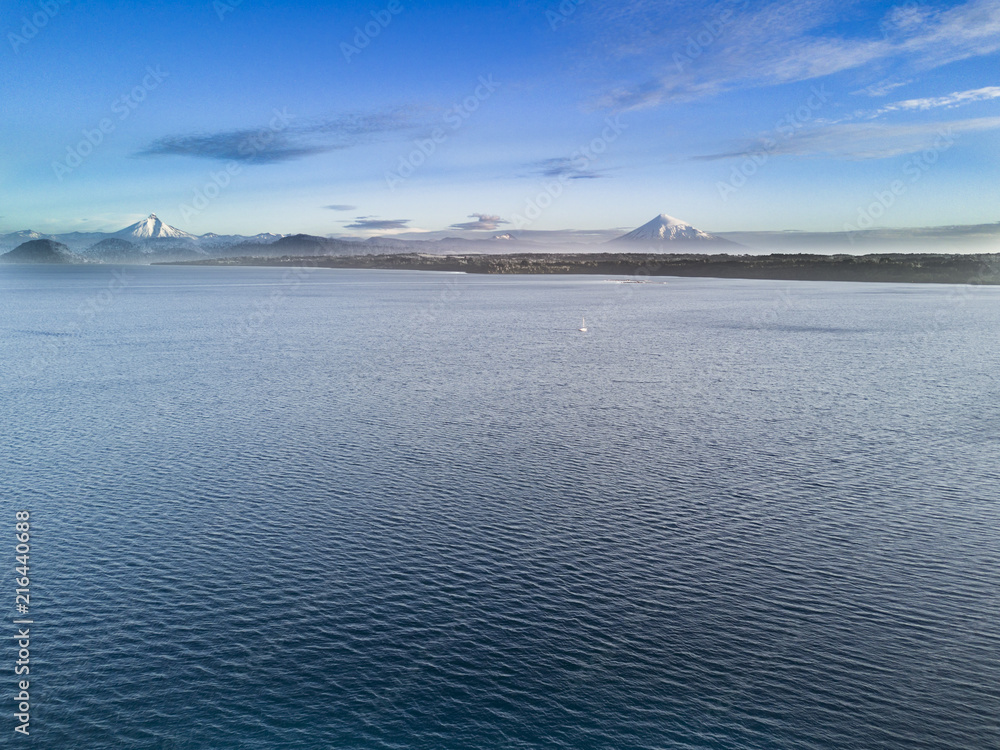 Rupanco Lake, one of the Great lakes in Southern Chile with an amazing aerial view from the drone over Osorno and Puntiagudo Volcanoes surrounded by the water and the trees during the sunset, Chile