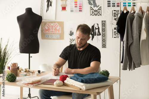 Serious male fashion designer drawing sketch of new clothes collection in ethnic design studio, man tailor creating line, working with brush or pencil on personal desk, developing embroidery pattern