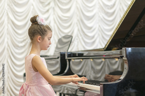 girl in a beautiful pink dress playing on a black grand piano. Girl playing on a black piano.