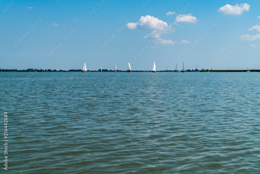 blauer See, am Horizont ein paar Segelboote und das Ufer