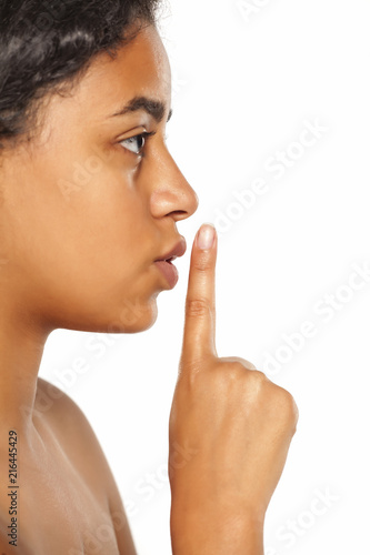 Closeup of a beautiful young dark-skinned woman with finger on her lips on a white background. Concept for silence