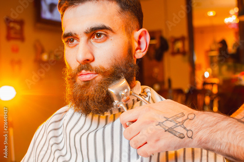 Barber cuts a beard of vintage hair clippers to a young handsome guy with a beard and mustache. Men s hair salon