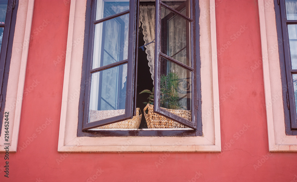 Half-opened window with flowerpots in a building with pink walls