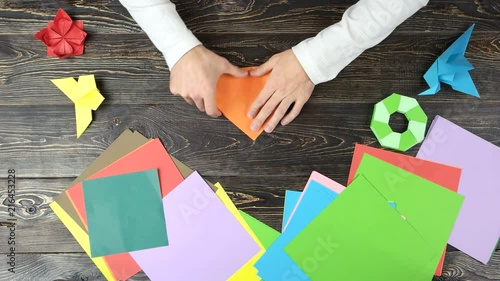 Folding origami paper in triangle, top view. Man making origami figures. Colourful papers. photo