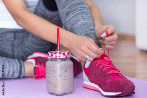 Attractive girl legs and detox smoothie in retro jar on purple yoga or fitness mat at home preparing red sneakers for trains. Sport and recreation concept. Close up, selective focus