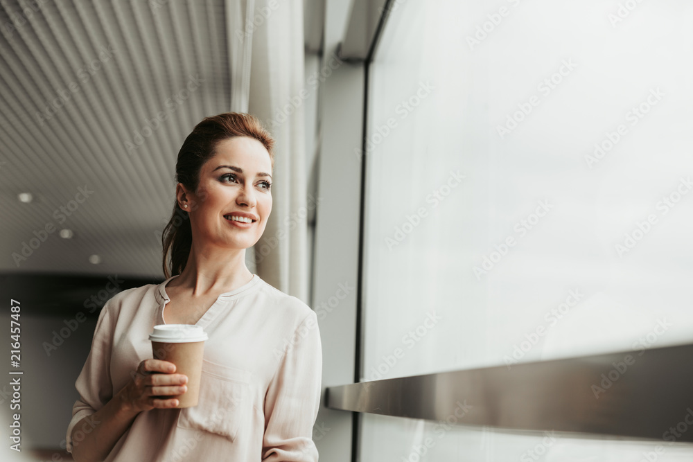 Portrait of beaming girl tasting mug of beverage while resting indoor at job Portrait of beaming girl tasting mug of beverage while resting indoor at job