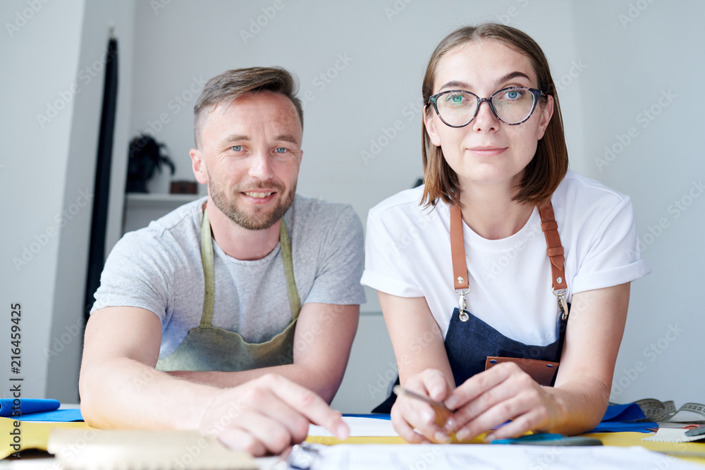 Portrait of two professional masters, man and woman, working at the table in workshop Portrait of two professional masters, man and woman, working at the table in workshop