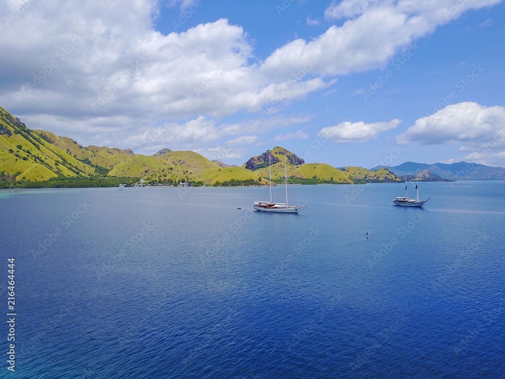 Obraz premium Aerial shot of beautiful blue lagoon at hot summer day with sailing boat. Komodo Island (Komodo National Park), Labuan Bajo, Flores, Indonesia.