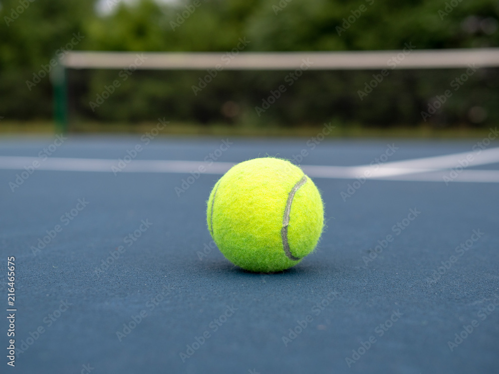 Tennis ball sitting on blue local tennis court with view close to ground 