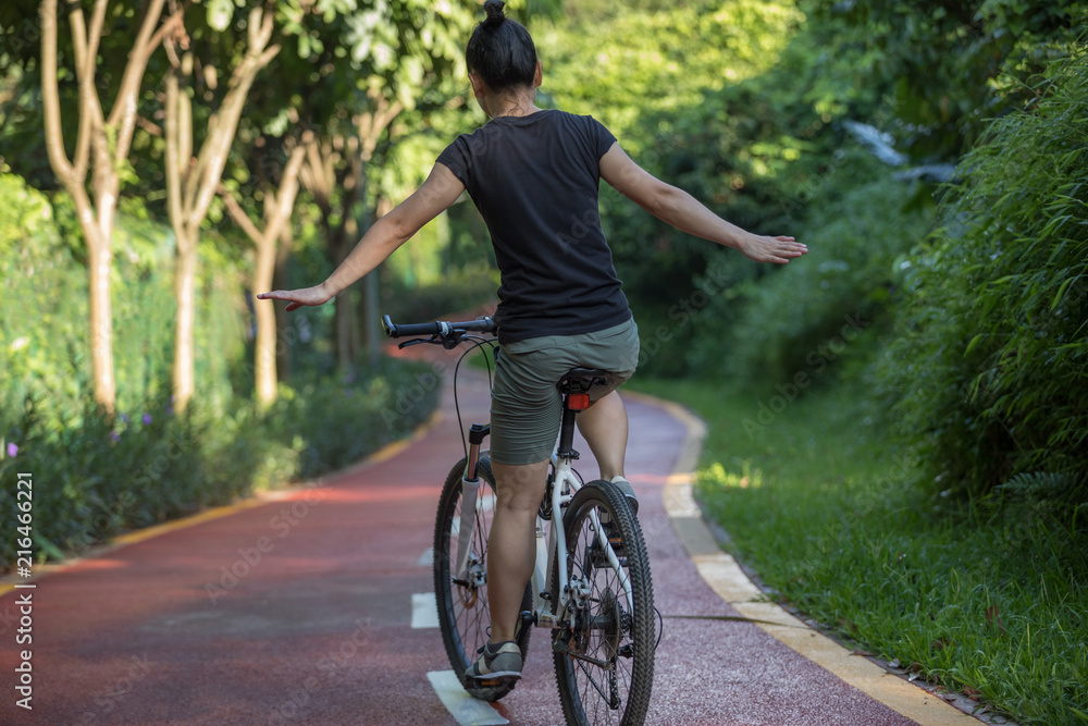 Naklejka premium Woman riding a bike on sunny park trail with arms outstretched