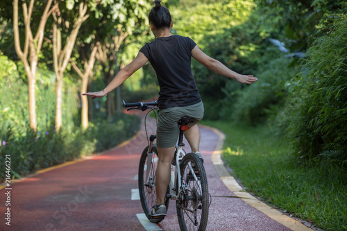 Woman riding a bike on sunny park trail with arms outstretched