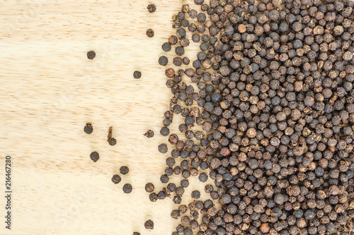 black peppercorns heap top view on wooden background.