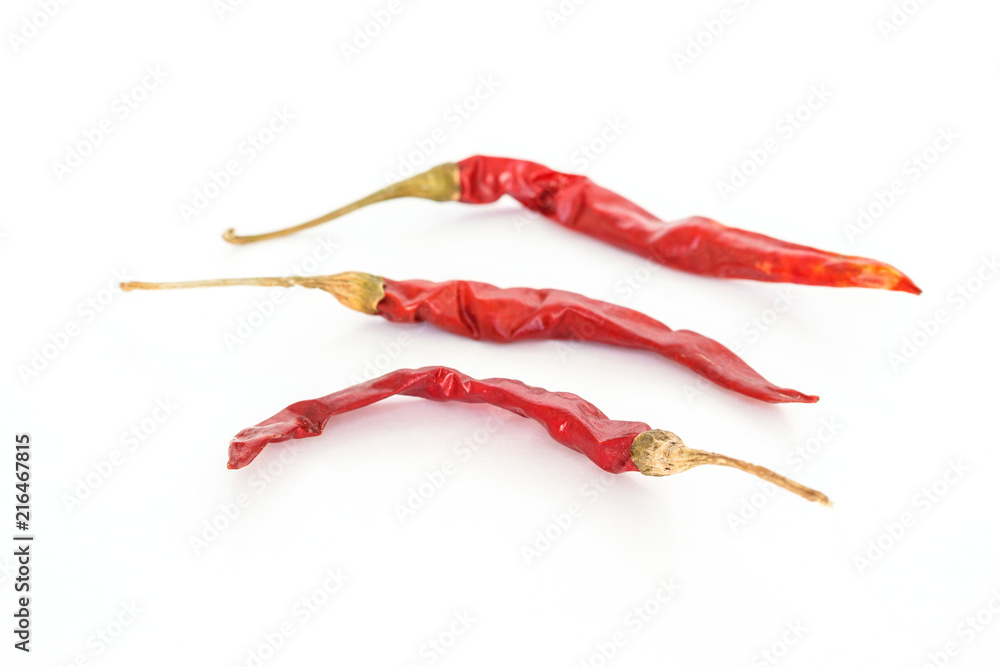 three red dried chilli peppers on white background.