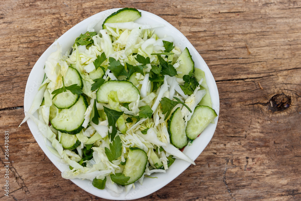 Spring vegan salad with cabbage, cucumber, green onion and parsley on wooden table. Top view Spring vegan salad with cabbage, cucumber, green onion and parsley on wooden table. Top view