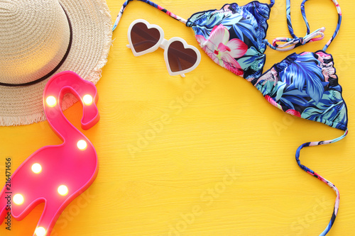 Top view of fashion female swimsuit bikini and hat over yellow wooden background. Summer beach vacation concept.