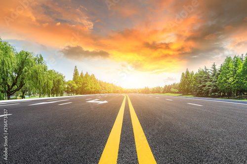 Asphalt road and green forest landscape at sunset