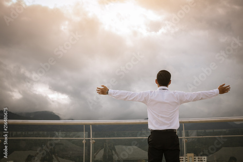 Businessman standing keeping arms raised and looking sky.
